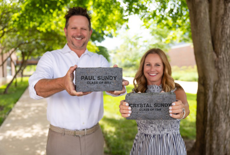 Paul and Crystal Sundy holding bricks engraved with their names and graduation years